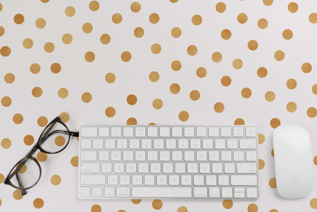 A keyboard, mouse, and glasses on a white and gold polka-dot background.
